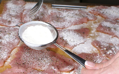 Schnitzel mit Weizenmehl Weizenmehl durch ein Sieb auf Schnitzel verteilen